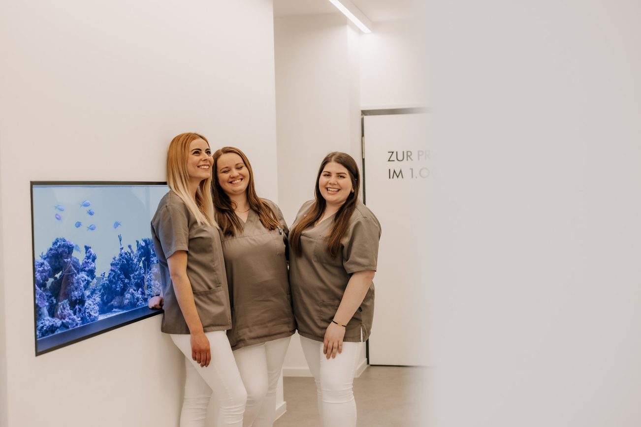 Drei Mitarbeiterinnen im Flur der Praxis vor dem Aquarium